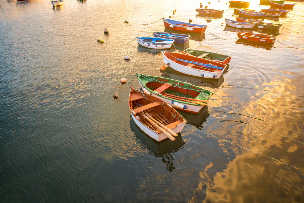 Small boats anchored on calm water at sunrise with reflections and mooring buoys