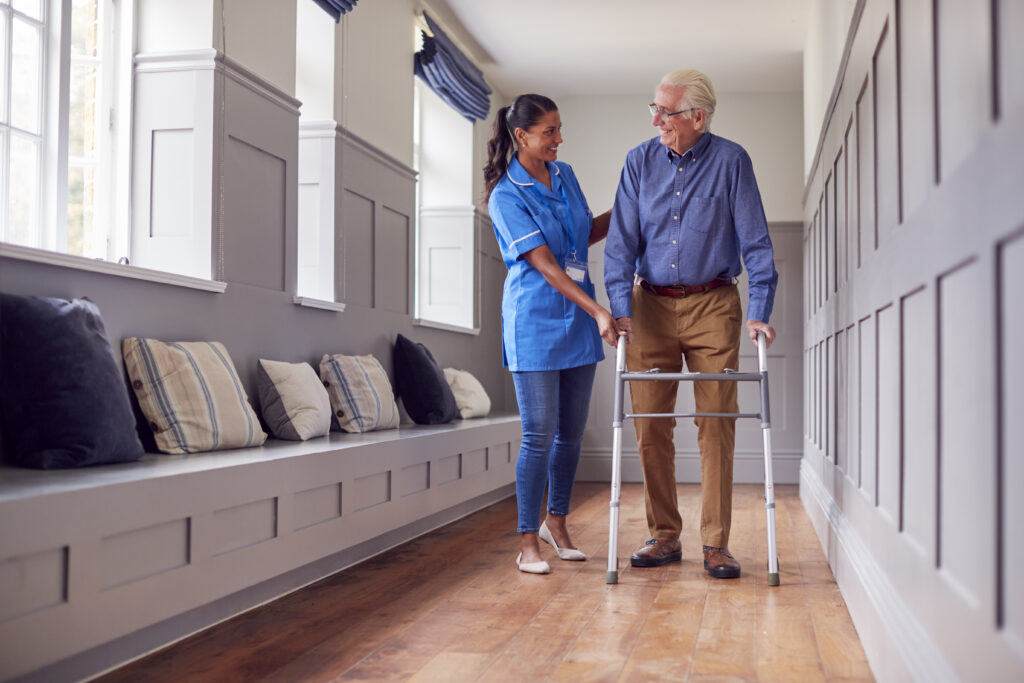Elderly resident walking with assistance in a nursing home hallway