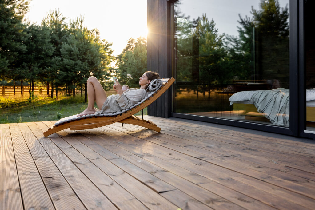 Airbnb guest relaxing on deck outside vacation rental home surrounded by nature and sunlight
